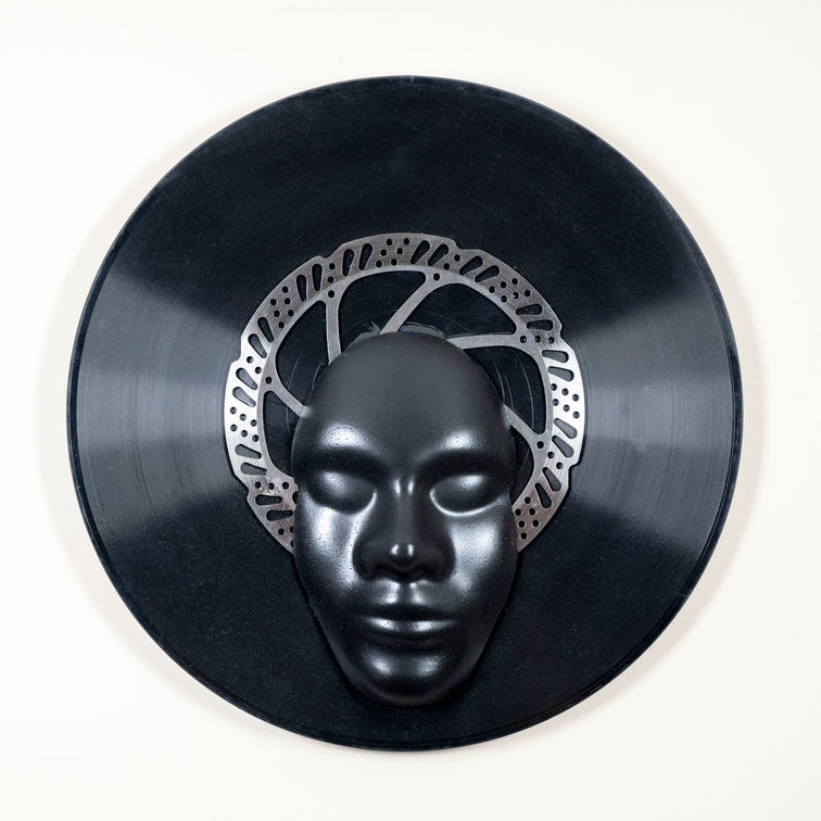 Disque vinyle noir avec un masque sculpté au centre.