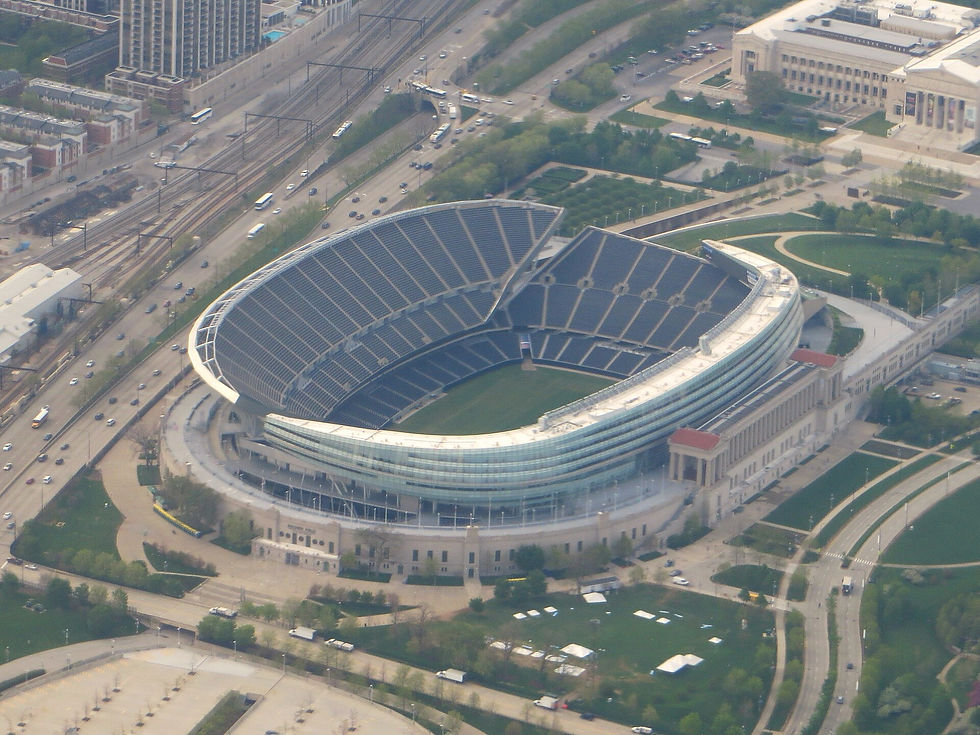 Aerial view of Soldier Field in Chicago, a bowl-shaped stadium with glass upper decks, surrounded by park land, rail lines and highway traffic