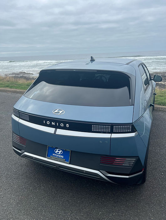 Light blue Hyundai Ioniq 5 rental parked above the Oregon coast, rear three-quarter view