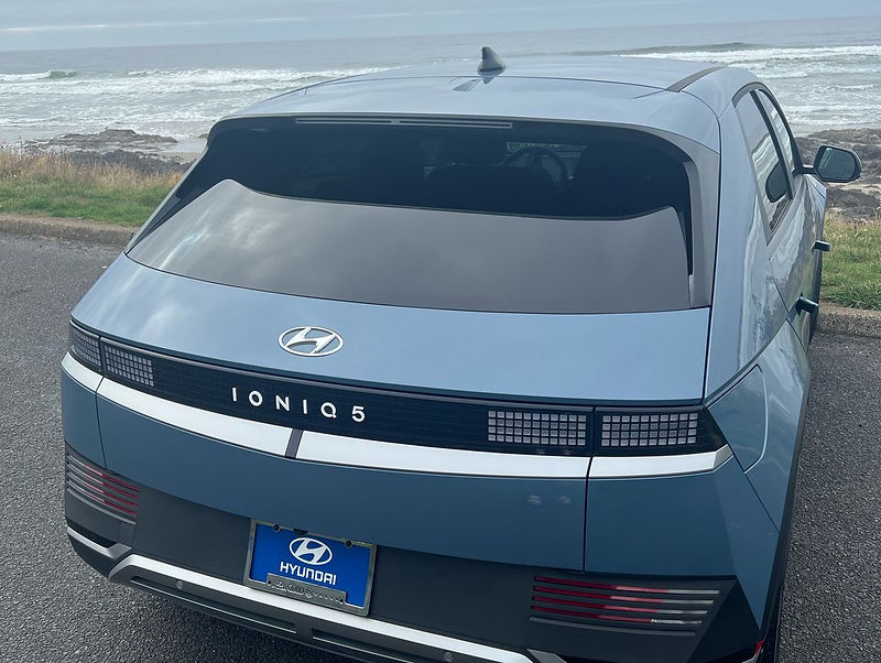 Light blue Hyundai Ioniq 5 rental from ORCritters parked above the Oegon coast, rear three-quarter view