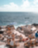 people lounging in beach chairs on a rocky beach with the sea in the background