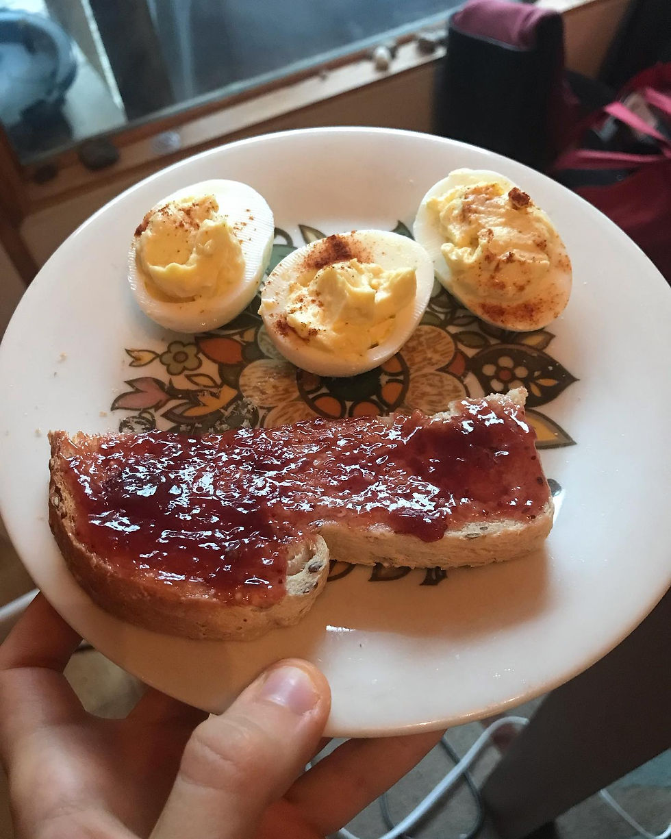 Three deviled eggs and half a piece of toast with strawberry jam