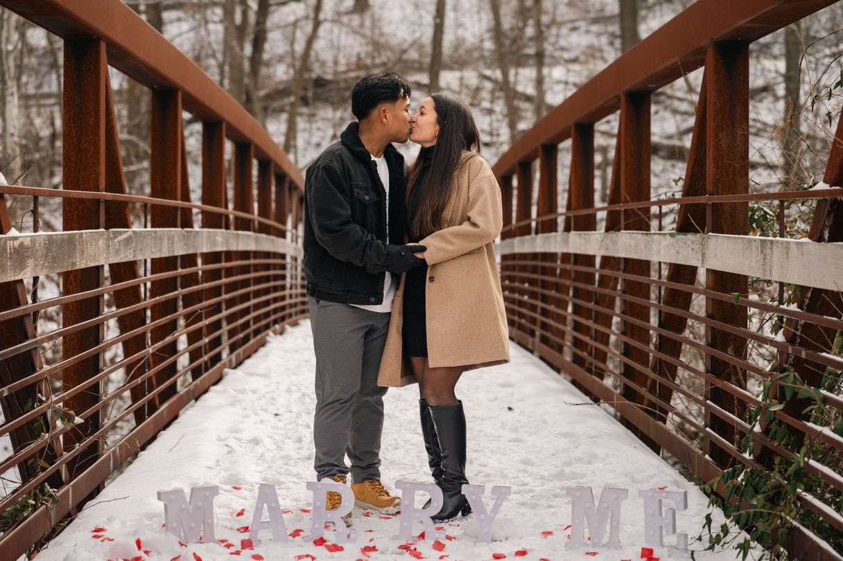 Newly engaged couple kissing on a snowy bridge