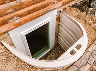 Basement egress window with white window well installed next to a home’s foundation, providing emergency exit, natural light, and proper drainage.