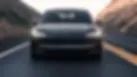 Coche Tesla oscuro conduciendo en carretera montañosa con faros encendidos.