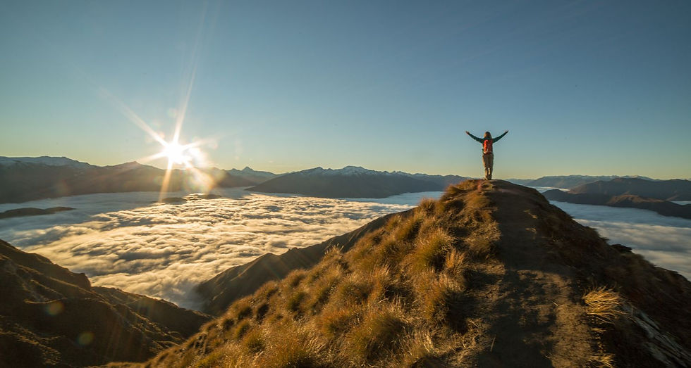 small business coach standing on the top of a grassy hill watching the sun rise over the clouds