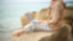 a small business owner working on their laptop while sitting on a rock near a beach