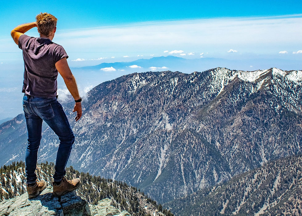 A hiker standing on a summit looking out over a mountain range