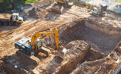 foundation excavation site with a backhoe and dump trucks.jpg