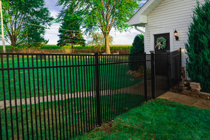 Black picket fence enclosing a green lawn next to a white house.