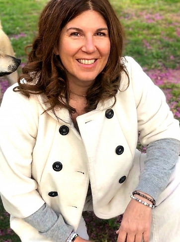 Nava owner of Pets Wit Nava, wearng a light-colored coat, sittig outdoors with light brown dog colo in the background