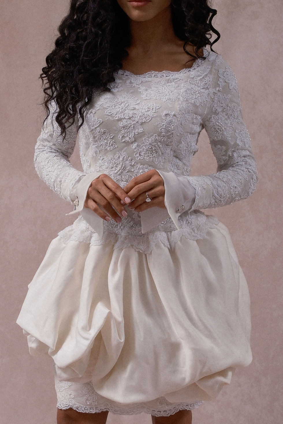Thumbnail: Curly haired model wearing vintage Christian Dior mini wedding dress with lace bodice in front of a beige backdrop