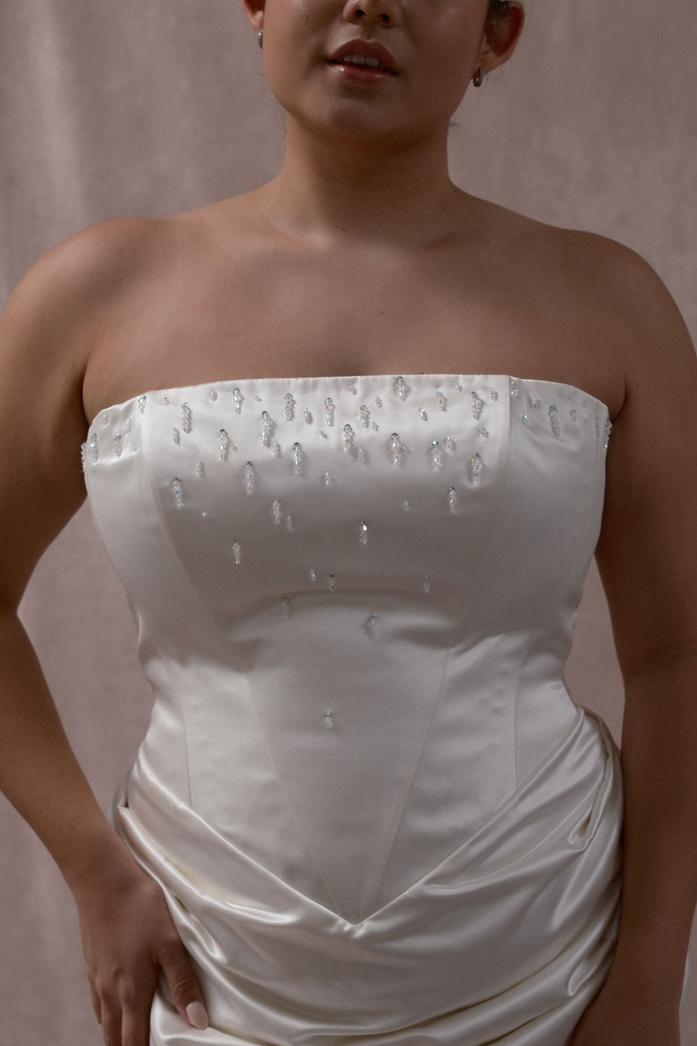 Thumbnail: Dark haired model wearing a plus size vintage wedding dress with beaded bodice against a beige backdrop