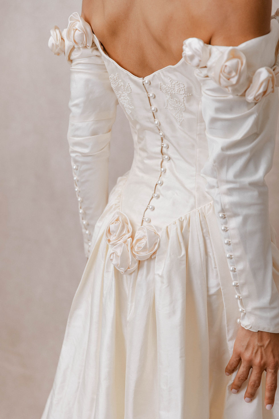 Thumbnail: Model showing back rosette detail of Catherine Rayner Louisa wedding dress against beige backdrop