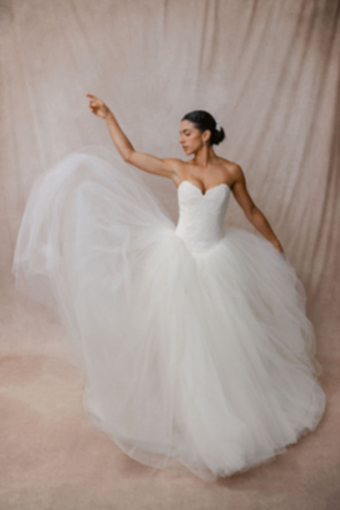 Model standing against beige backdrop tossing the skirt of the Vera Wang Bride Wars wedding dress