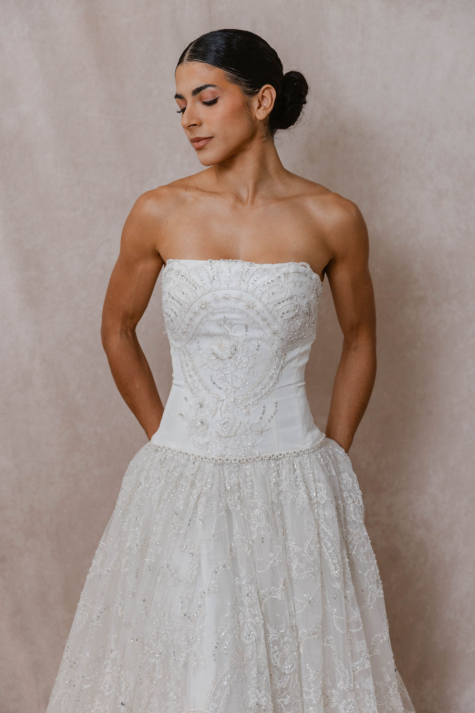 Dark haired model wearing a beaded vintage wedding dress against a beige backdrop