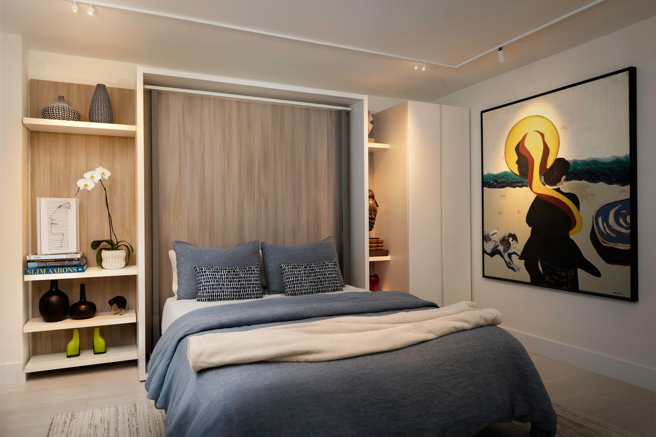 The same den transformed into a guest bedroom with a queen-size bed, blue bedding and contemporary art.