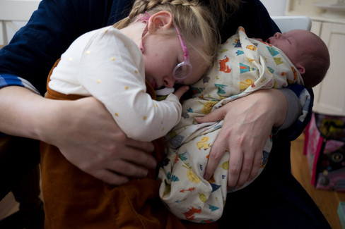 Toddler snuggles with newborn baby in mom's arms