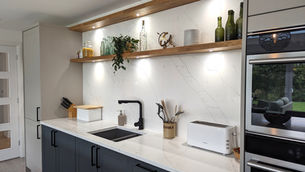 Modern kitchen with marble backsplash, open shelves with bottles, and a plant. White toaster and utensil holder on the counter.