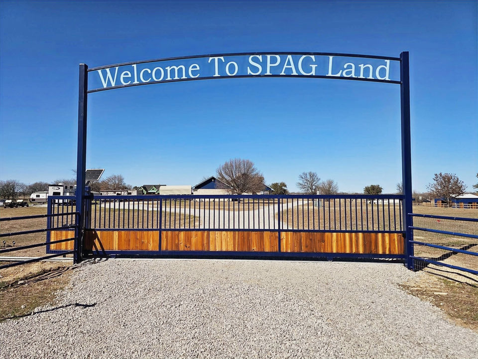 Custom ranch entry slide gate with metal frame and cedar wood panels reading Welcome To SPAG Land