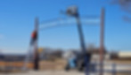 Workers installing a large metal entrance sign reading ‘Welcome to SPAG Land’ using a lift and ladder at a rural property entrance