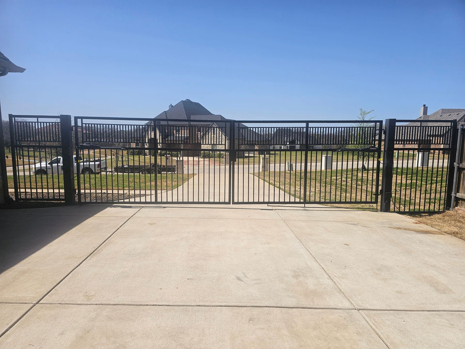 Custom metal sliding driveway gate being installed at residential property with house and driveway in background