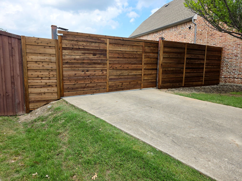 Horizontal wood sliding driveway gate on installed along residential backyard fence