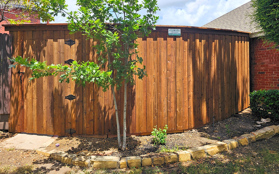 Stained cedar wood privacy fence with gate installed along curved backyard landscape
