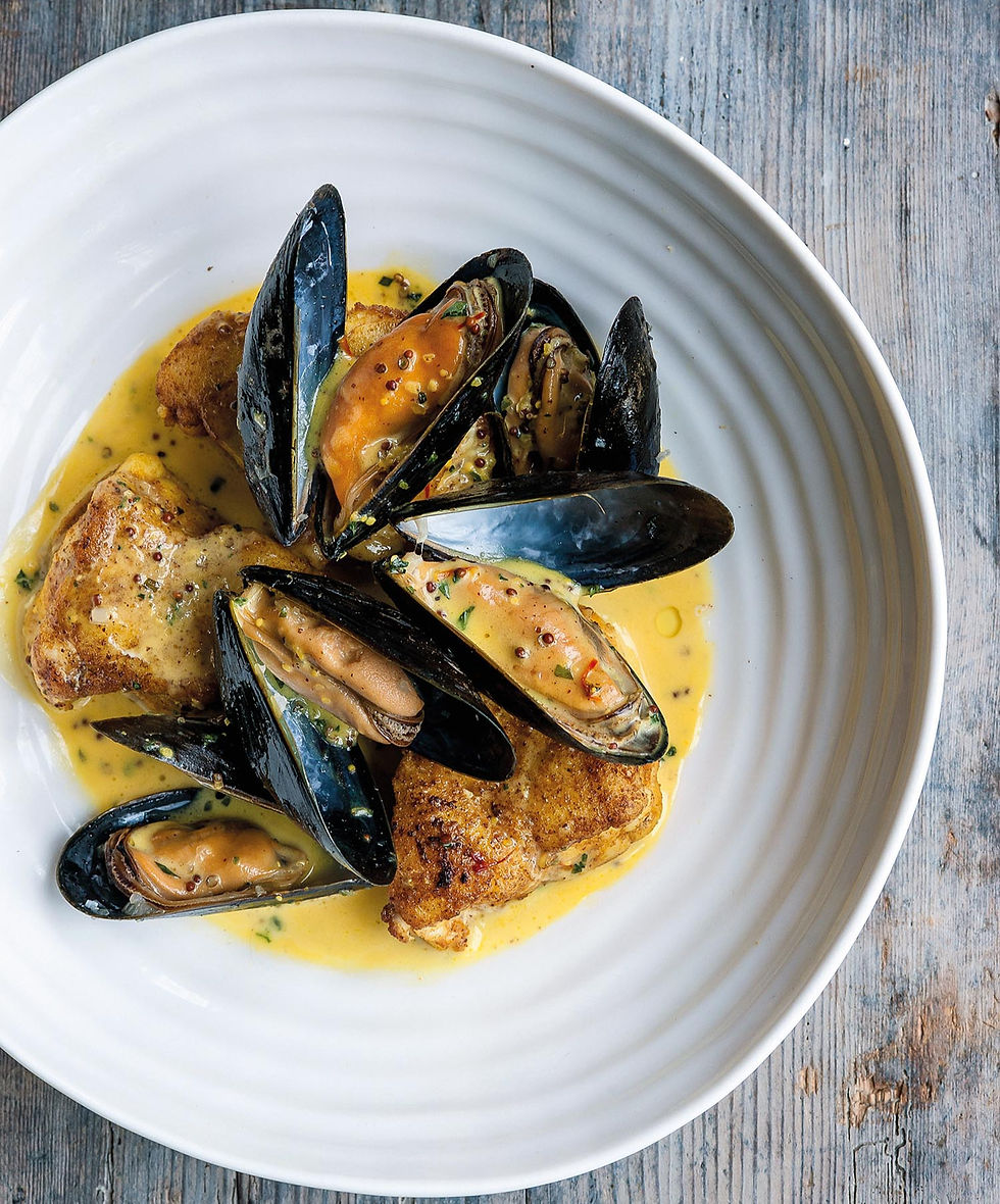 Mussels and seared fish in creamy yellow sauce on a white plate, shot overhead on a weathered blue wooden table. Pan-fried monkfish with mussels and a grain mustard tarragon sauce recipe