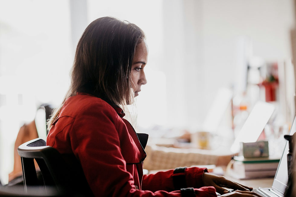 A woman in a red jacket types on a laptop, focused and intent. The blurred bright background suggests an office setting.