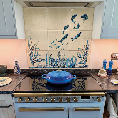 Blue pot on black stove in a kitchen, with fish-and-seaweed tile backsplash and blue/white decor; ESTEL on oven front.