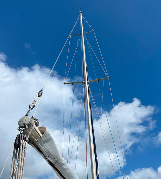 Sailboat mast and boom against a bright blue sky with fluffy white clouds.