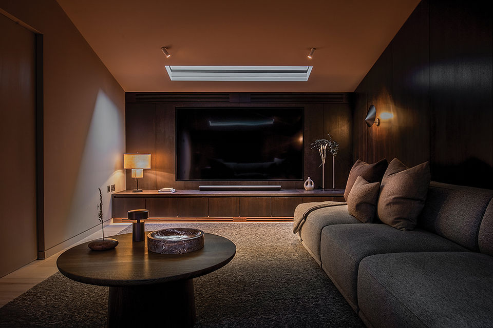 Warm modern living room with large TV, gray sofa, round coffee table, and soft amber lighting.