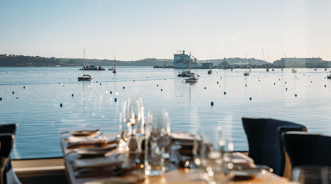 Table set for dining, with a clear view of a calm harbor. Boats float gently under a blue sky, creating a serene atmosphere.