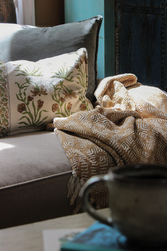 Close-up of a floral cushion and woven throw on a sofa, with a ceramic mug blurred in the foreground.