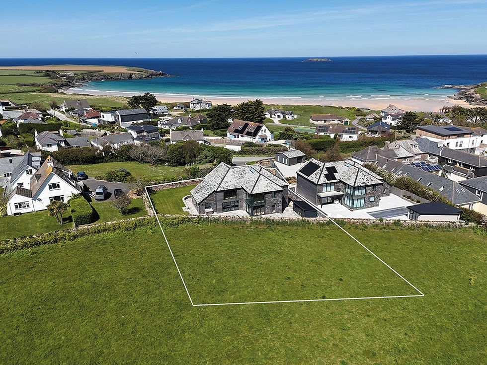 Aerial view of a coastal village with modern houses, sandy beach and blue sea, highlighting an empty outlined grassy lot.