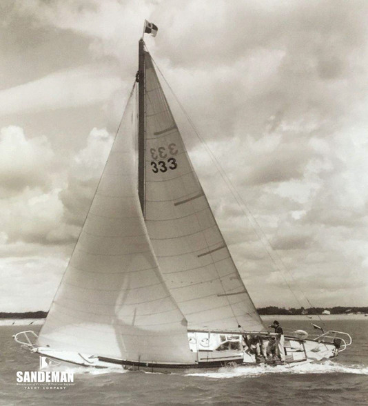 Sailboat racing on choppy water under cloudy sky, mainsail marked 333, with SANDEMAN YACHT COMPANY logo.