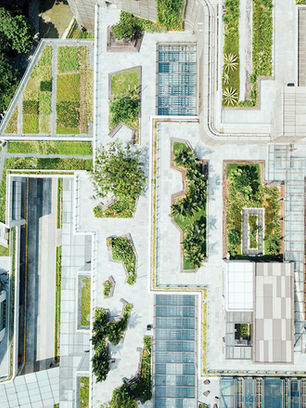 Aerial view of a modern rooftop garden complex with geometric planters, glass roofs, and walkways amid tall buildings.