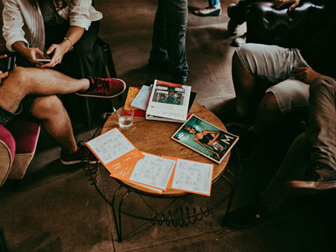 A group of people in an informal creative meeting, with magazines and printed documents on the table alongside smartphones, reflecting the integrated marketing approach of Leven Media Group