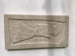Rectangular stone relief sculpture by Richard Holliday showing an abstract fish form set against a textured carved background.