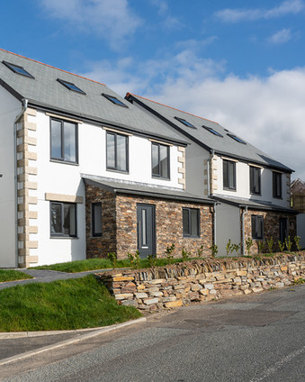 Modern semi-detached houses with gray roofs, stone and white facades, under a blue sky beside a quiet street.