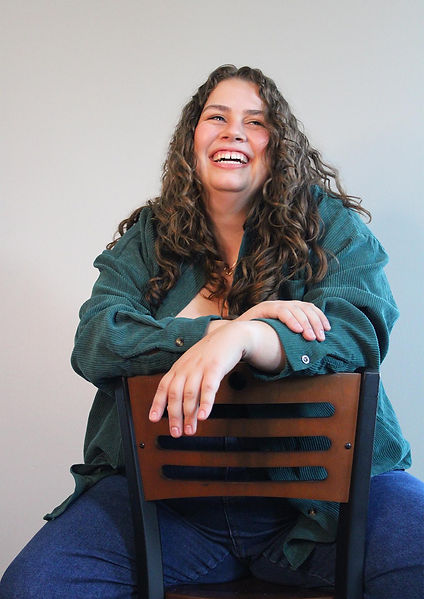 woman with long brown curly hair laughing backwards on a chair