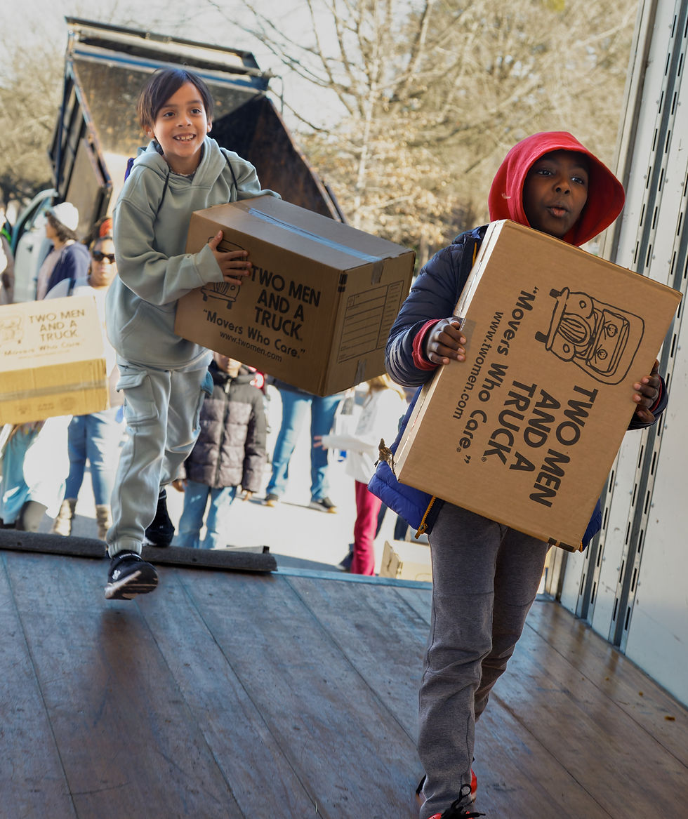 Two smiling children carry boxes into a moving truck.