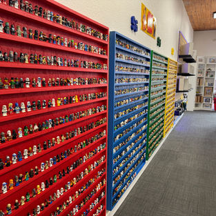 A wall of different colored shelves displaying LEGO minifigures for sale at Brick Heads Haines City Florida
