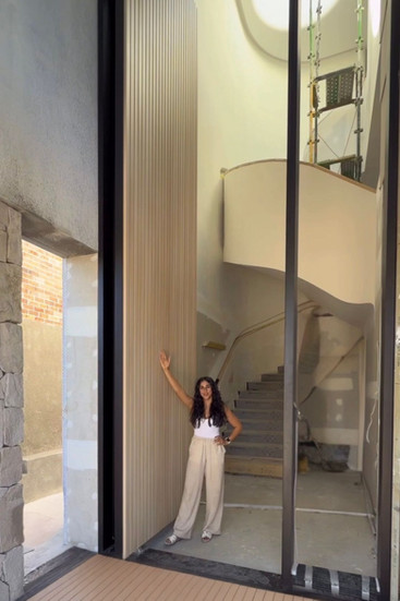 a lady standing next to a very big wood like finish aluminium pivot door