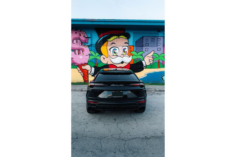 Black Lamborghini Urus parked in front of a colorful mural featuring cartoon artwork.