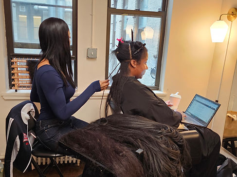 Hairstylist of nadia vassell salon sitting a doing a customer's hair, while the customer finishes work on her laptop