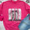Thumbnail: Pink sweatshirt featuring a cowgirl praying graphic with the words “This Cowgirl Prays,” styled with jeans on a brick backgro