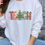 Thumbnail: White sweatshirt with colorful TEACH design featuring leopard print letters and a Christmas tree.