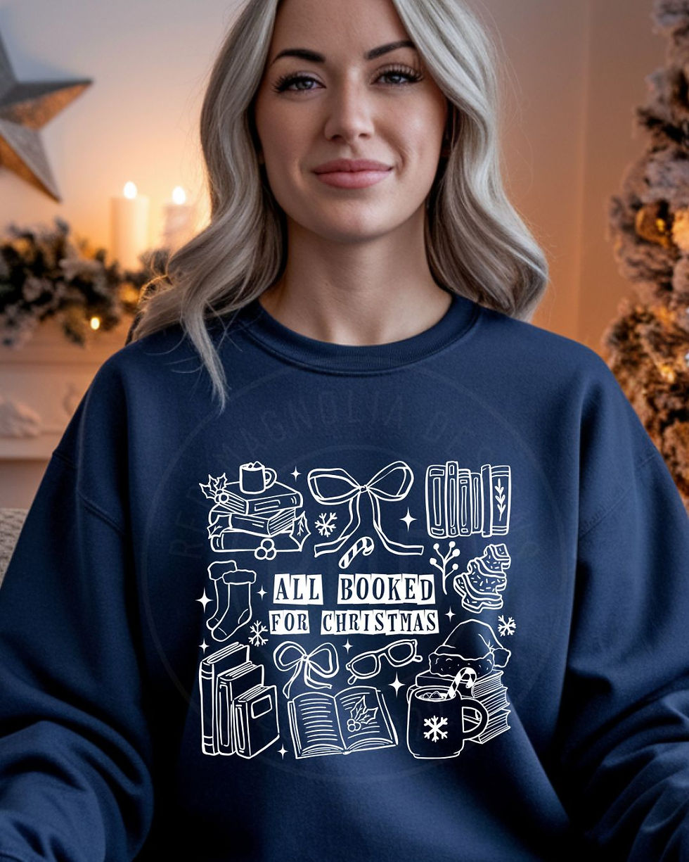 Navy sweatshirt with white outline Christmas and book-themed doodles and the phrase “All Booked for Christmas.”